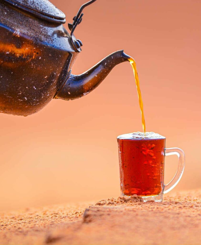 Das Bild zeigt eine Teekanne Tee eingießend in eine Glastasse mit Heilfasten Tee