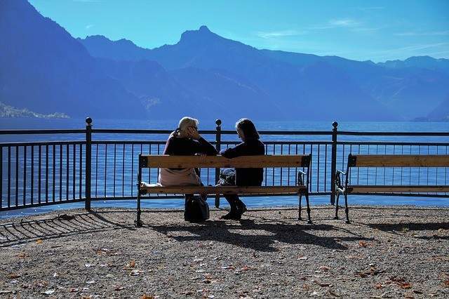 Zwei Frauen auf einer Bank reden miteinander, im Hintergrund sind Berge zu sehen